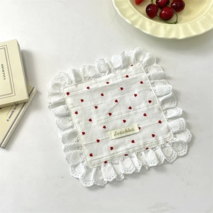 Detail view of square white cotton napkin with red heart patterns and lace edging