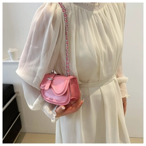 Close-up of pink mini saddle bag with silver chain strap worn by model on white skirt