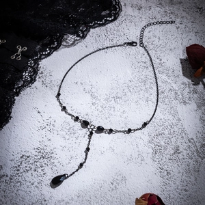 Detailed view of Gothic black choker with blood drop tassels on a stone background