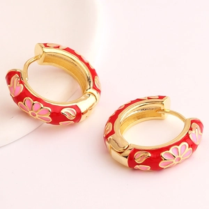 Detailed close-up of golden huggie hoops with red enamel and pink floral patterns