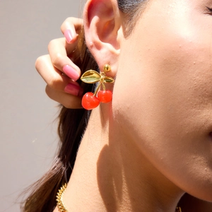 Detail showing red cherry pendant earrings with golden leaves worn by a model