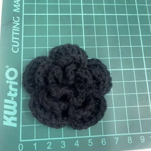 Detailed top view of 7cm black hand-crocheted 3-layer flower on a green cutting mat