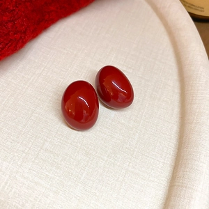 Close-up of elegant deep red oval stud earrings with high-gloss finish on ivory tray