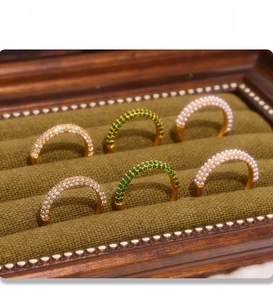 Detail of PVD electroplated gold rings with zircon, green gemstone and pearls in a box