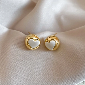 Detailed close-up of golden heart-shaped stud earrings on champagne silk fabric