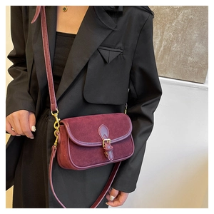 Close-up of burgundy suede crossbody bag with gold buckle on a model in a black suit
