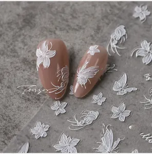 Macro shot of 3D embossed white butterfly and floral nail art stickers on nude base