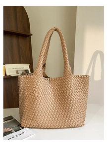 Close-up of a large light brown hand-woven tote bag on a white table in a warm room