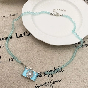 Detail van lichtblauwe kralenketting met camera-hanger en parelmoer inleg in de lens