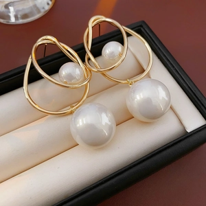 Detail of gold geometric earrings with large imitation pearl pendants in a black jewelry box