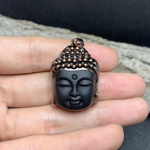 Close-up of matte black Buddha head pendant with bronze metallic accents on hand