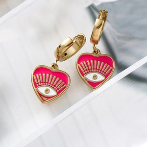 Detail shot of heart-shaped gold earrings with pink enamel and evil eye pattern
