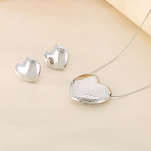 Détail du pendentif cœur argenté et boucles d'oreilles assorties sur fond en tissu beige