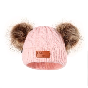 Detailed knit texture of pink baby beanie with dual faux fur pom-poms and leather patch
