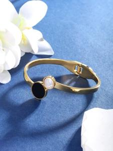 Detail of gold-tone open bangle featuring black and white shell circular inlay detail