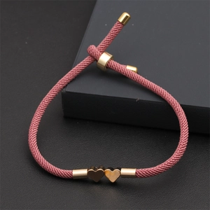 Detailed view of adjustable pink woven Milan rope bracelet with two gold heart charms