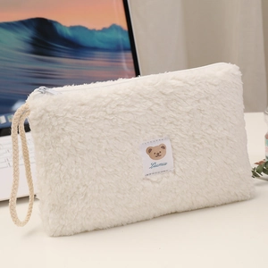 Detail view of the soft white plush cosmetic bag with a cute bear label and top zipper