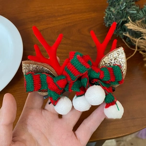 Christmas plush reindeer antler hair clips with red and green striped knit bow on a girl's hand
