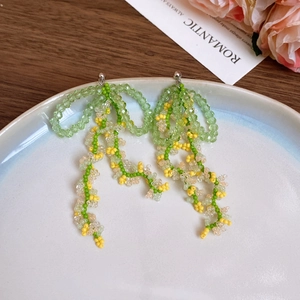 Macro detail of handmade green and yellow beaded tassel earrings on a white ceramic tray