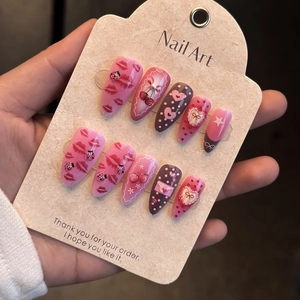 Detail of pink almond press-on nails featuring cherry, heart, and lip art designs