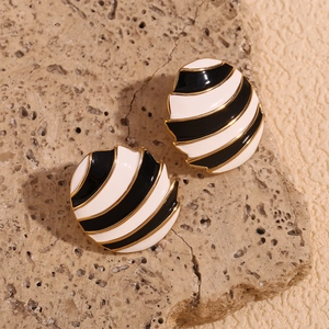 Close-up of gold-plated oval stud earrings with black and white enamel spiral pattern