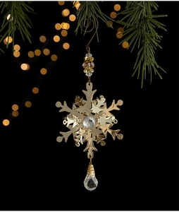 Detailed view of golden metal snowflake ornament with crystals hanging on a pine branch