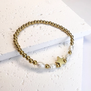 Detailed close-up of golden beads, baroque pearls and star charm on a stone surface