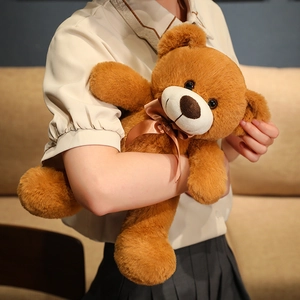 Classic brown plush teddy bear toy with dark ribbon bow held by a model in a home setting