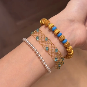 Detail of layered gold beaded bracelets with blue gemstones and classic white pearls
