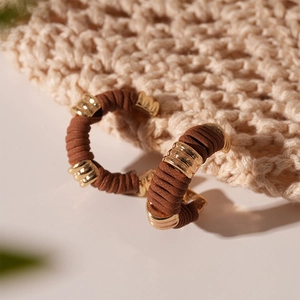 Détail de boucles d'oreilles C en cuir marron avec anneaux dorés sur un tapis tissé