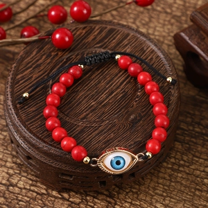 Close-up of red beaded bracelet with blue evil eye pendant on a vintage wood tray