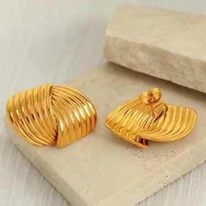 Elegant gold titanium earrings with textured wave design on a minimalist stone tray