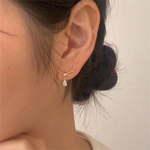 Detailed close-up of a golden bow earring with a sparkling pear-shaped zircon on a model