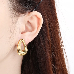 Close-up of gold hollow teardrop earrings with spiral texture worn by a model
