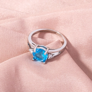 Detailed view of silver ring with blue center stone on soft pink silk fabric background