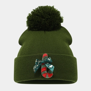 Detail of green Christmas beanie with large pompom, candy cane patch and festive bow