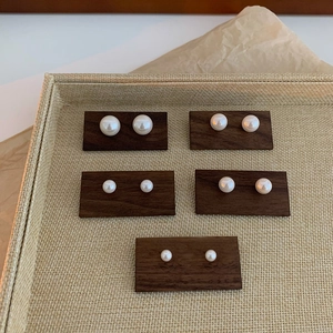 Five pairs of elegant white pearl stud earrings in various sizes on wood display