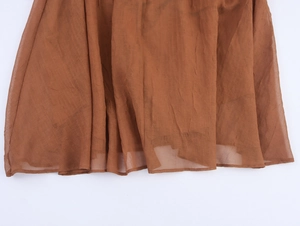 Detailed macro view of caramel brown pleated chiffon fabric showing sheer texture and drape