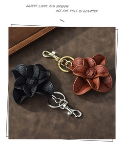 Close-up of leather camellia flower keychains in black and brown with metal buckles