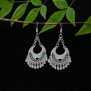 Detailed view of vintage silver tassel earrings with green glaze on a dark branch
