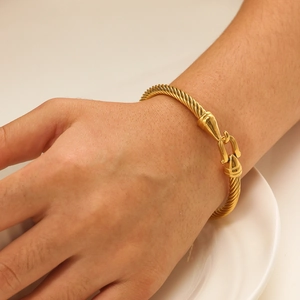 Detail of a gold twisted cable bracelet with a U-shaped shackle clasp on a wrist