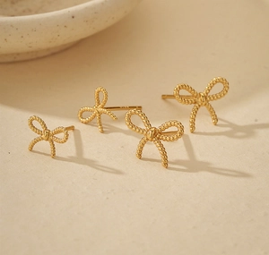 Close-up of gold bow earrings in two sizes on beige ceramic and linen background