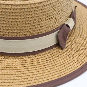 Close-up of woven straw hat featuring a dark brown ribbon bow and detailed edging
