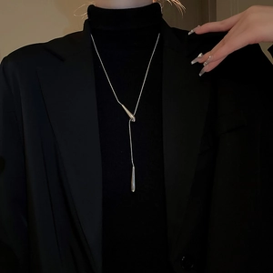 Detail shot of a silver water drop pendant necklace on a black turtleneck sweater