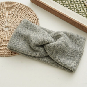 Detail of light grey knitted headband featuring a cross-knot design and wool texture