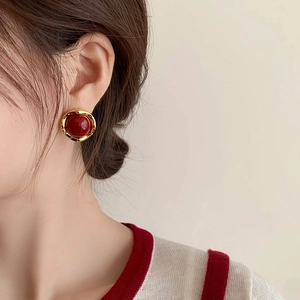 Dettaglio dell'orecchino tondo in smalto rosso con bordo dorato indossato da una modella