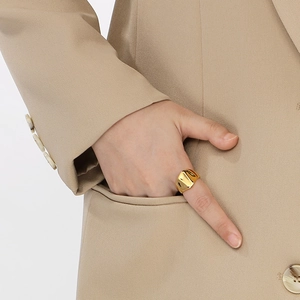 Close-up of a wide gold-plated lava ring on a model hand with beige blazer detail