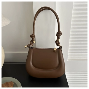 Detail of a brown leather shoulder bag with twisted rope strap and gold zipper