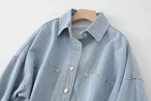 Detailed view of light blue denim jacket featuring metal buttons and chest pockets
