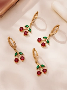Détail de boucles d'oreilles cerises dorées avec pierres rouges et feuilles vertes